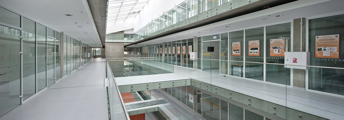 &Scaron;iuolaikinė vidaus architektūra su stiklinėmis pertvaromis, atviromis erdvėmis ir natūralia &scaron;viesa. Vaizdas perteikia modernų, atvirą ir struktūruotą pastato dizainą.