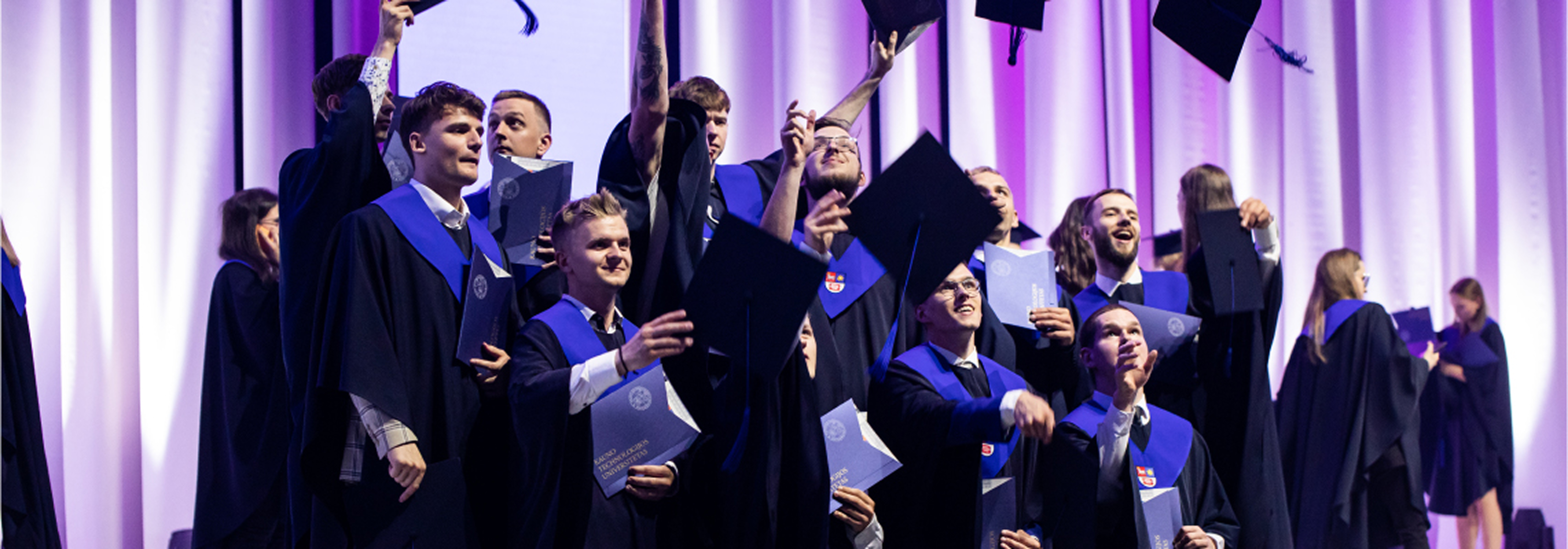 Baneris – Įtraukiantis, transformuojantis ir įgalinantis mokymasis ateičiai Studentų diplomų įteikimo šventė. Absolventai džiaugsmingai meta akademines kepures į orą laikydami diplomus. Vizualas atspindi įtraukiantį, transformuojantį ir įgalinantį mokymąsi ateičiai.