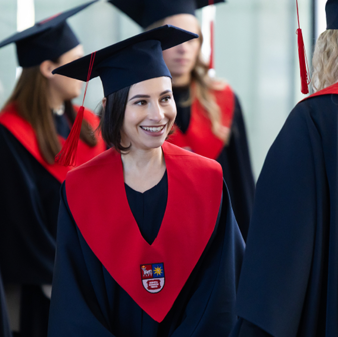 Laukiami rezultatai - Įtraukiantis, transformuojantis ir įgalinantis mokymasis ateičiai Absolventė su akademine mantija ir diplomu diplomų įteikimo ceremonijoje. Vizualas atspindi studijų sėkmę, kompetencijų ugdymą ir pasirengimą kurti ateities pokyčius.