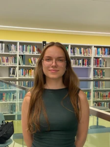 KTU studentė Gustė Lastauskaitė pozuoja prie&scaron; fotoobjektyvąm fone matosi knygų lentynos