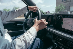 Vyras vairuoja automobilį, rankos laiko vairą, šone matosi navigacija